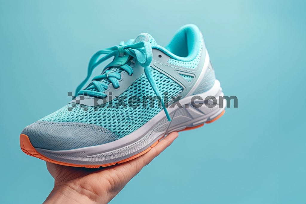 Hand holds running sneakers on blue background image.