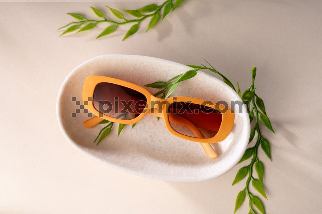Yellow sunglass on podiums and green leaves image.