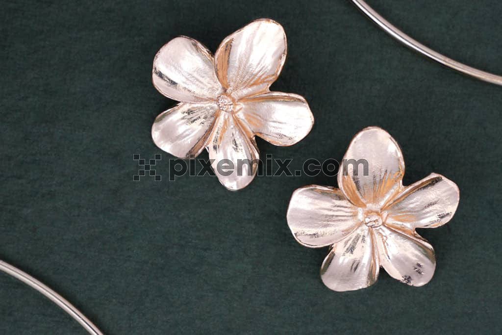 Close up of flower design earrings on green background image.