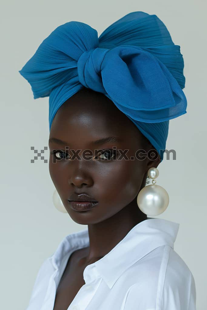 A beautiful black woman wearing a blue bow on her head and big pearl jewellery on her ears.