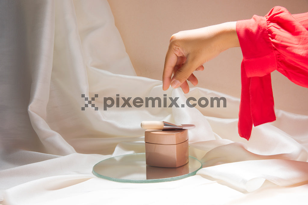 A hand picking up beauty product on satin fabric background with soft natural light stock image.