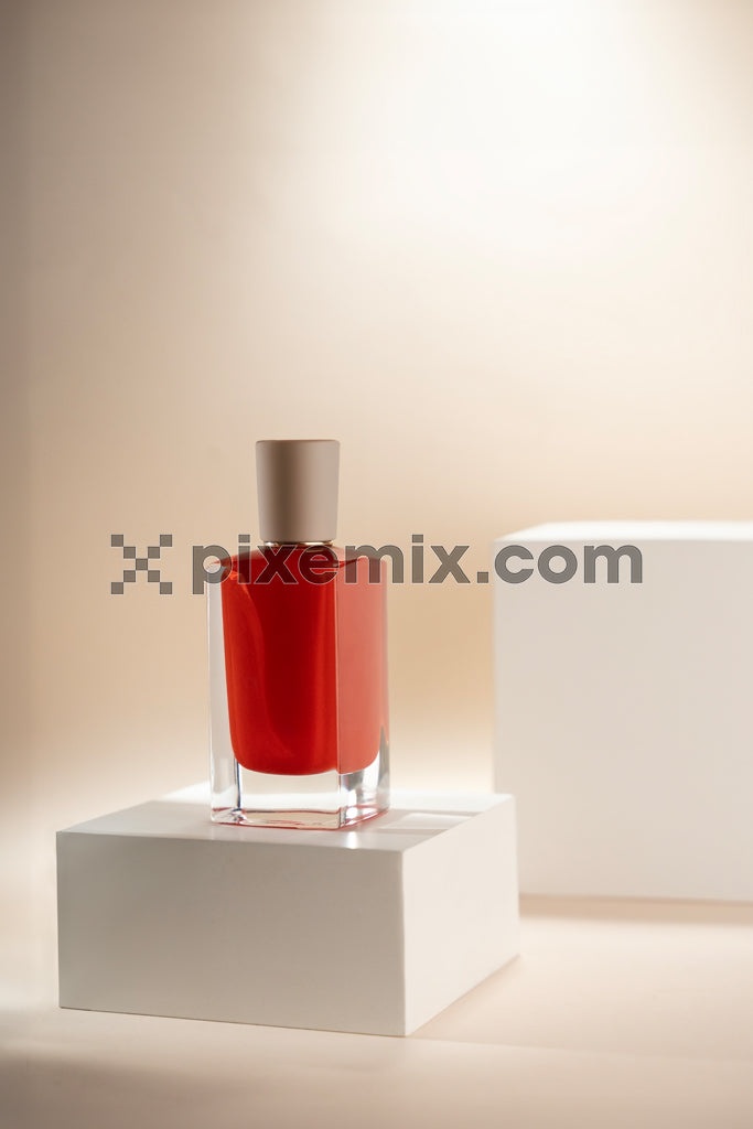 Minimalist red nail polish bottle on white display pedestal with elegant soft lighting and shadows stock image.