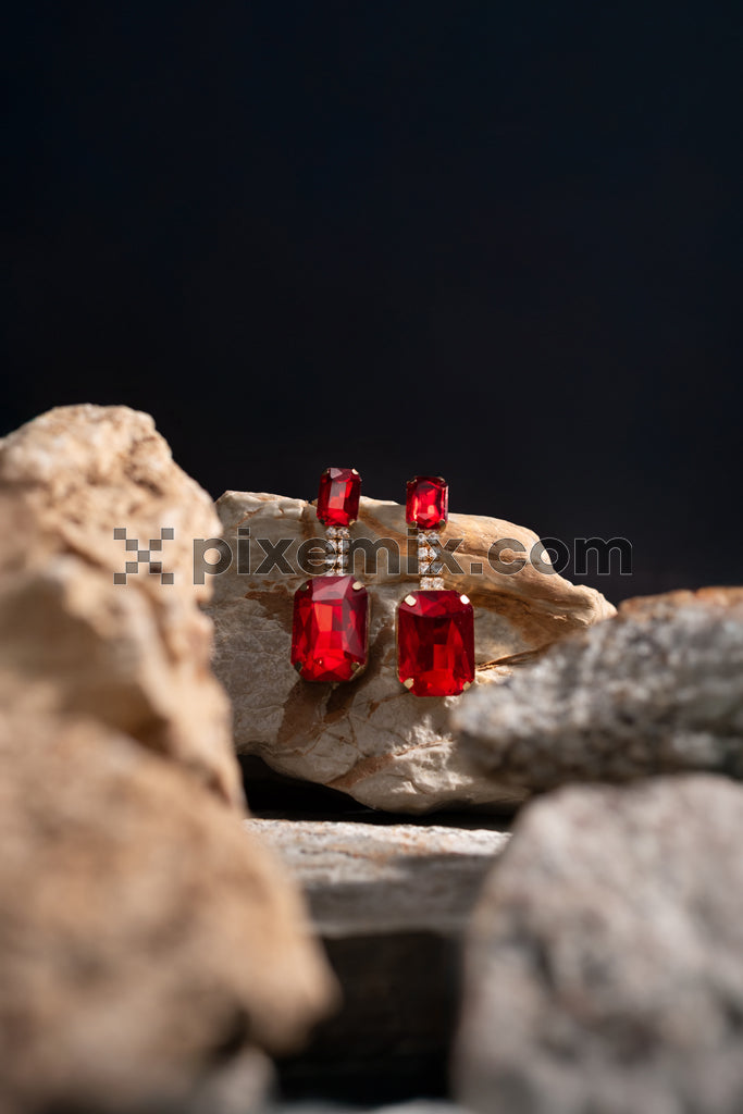 Luxuryruby gemstone earrings displayed on natural rocks with dramatic lighting stock image.