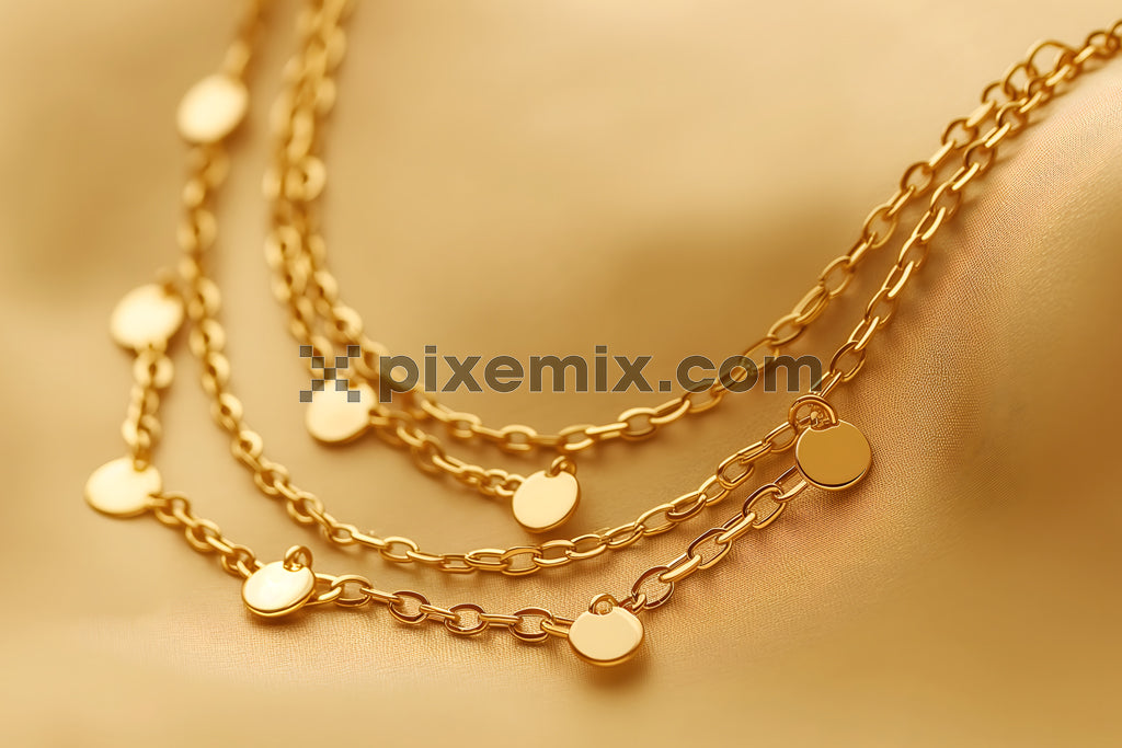 Elegant gold chain necklace with round pendants on golden satin fabric background.