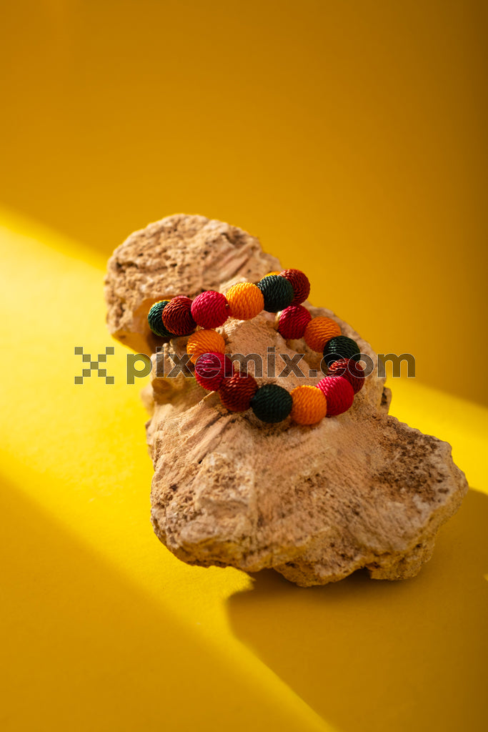 Handmade colorful bead bracelet on coral rock with vibrant yellow background stock image.