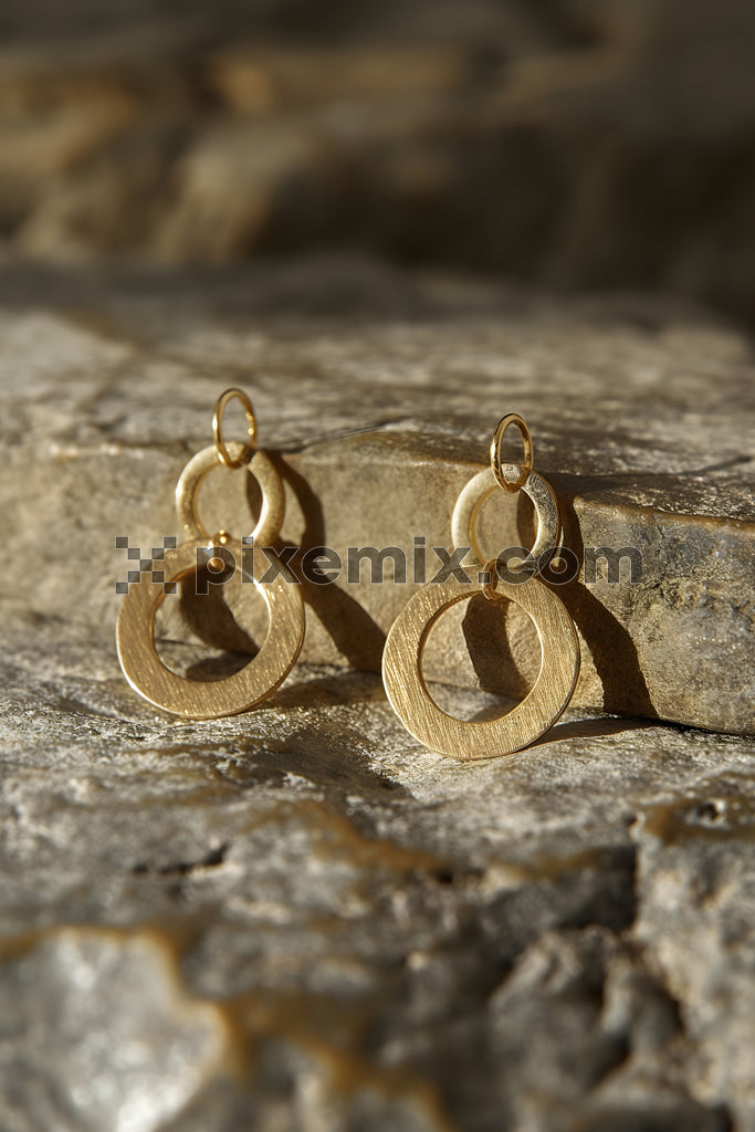 Minimalist gold hoop earrings displayed on textured stone surface with natural lighting stock image.