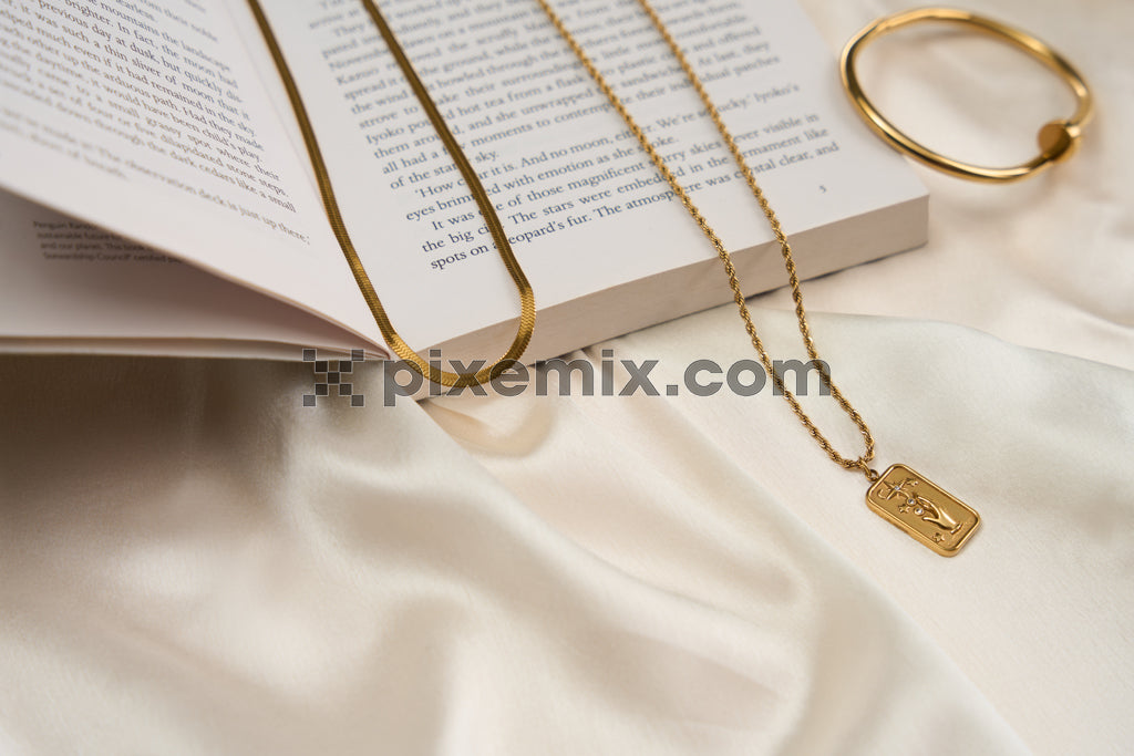 Elegant gold jewelry on satin fabric with open book creating a luxurious flat lay scene.