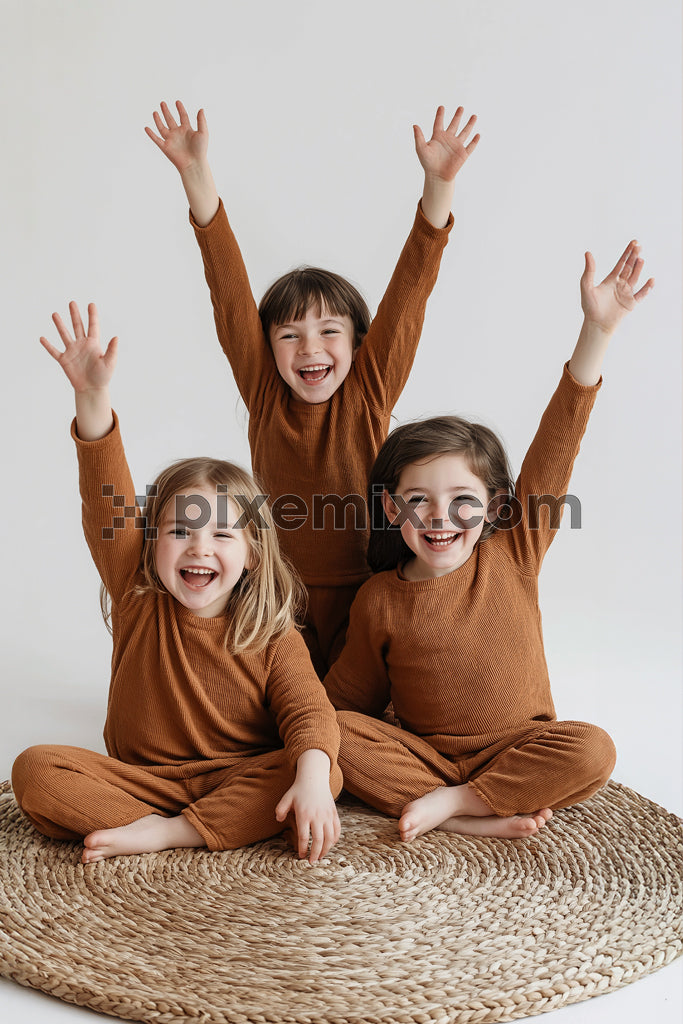 Three joyful children sitting on a rug with hands raised stock image.