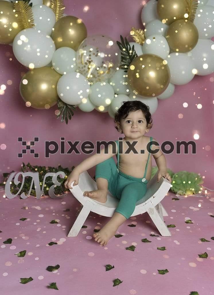 Happy indian kid sitting on a wodden chair turning one image with birthday balloons in the background image