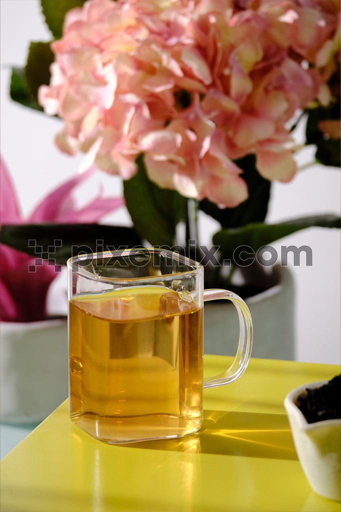 A delicate pink flower rests beside a steaming glass mug image.