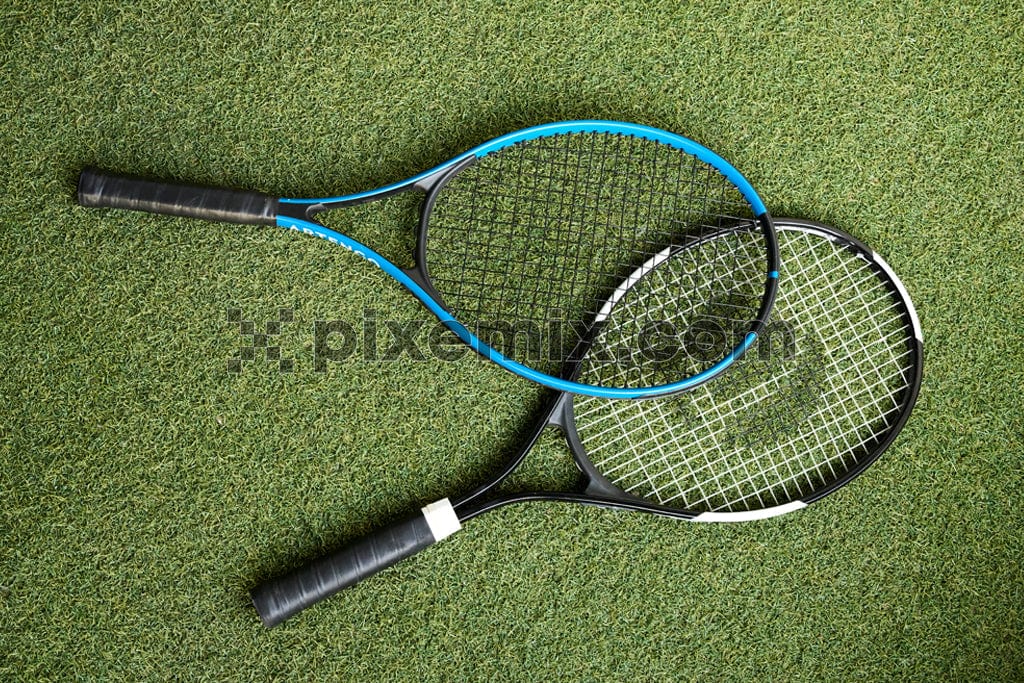 Two tennis rackets lie side-by-side on a green tennis court image.